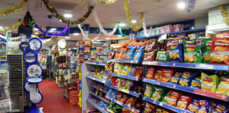 A shop floor with crisps on the shelves to the right and tinsel hanging from the roof.