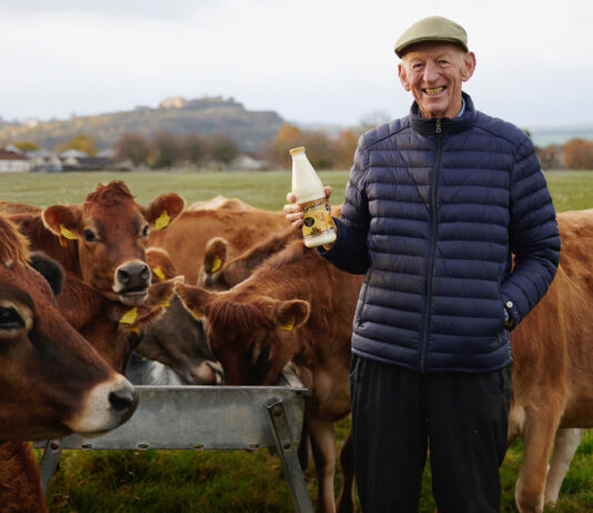 Graham’s goes for Gold this Christmas Dr Robert Graham stands in a field holding a bottle of Graham's Jersey Milk with the family's herd of cows behind him.