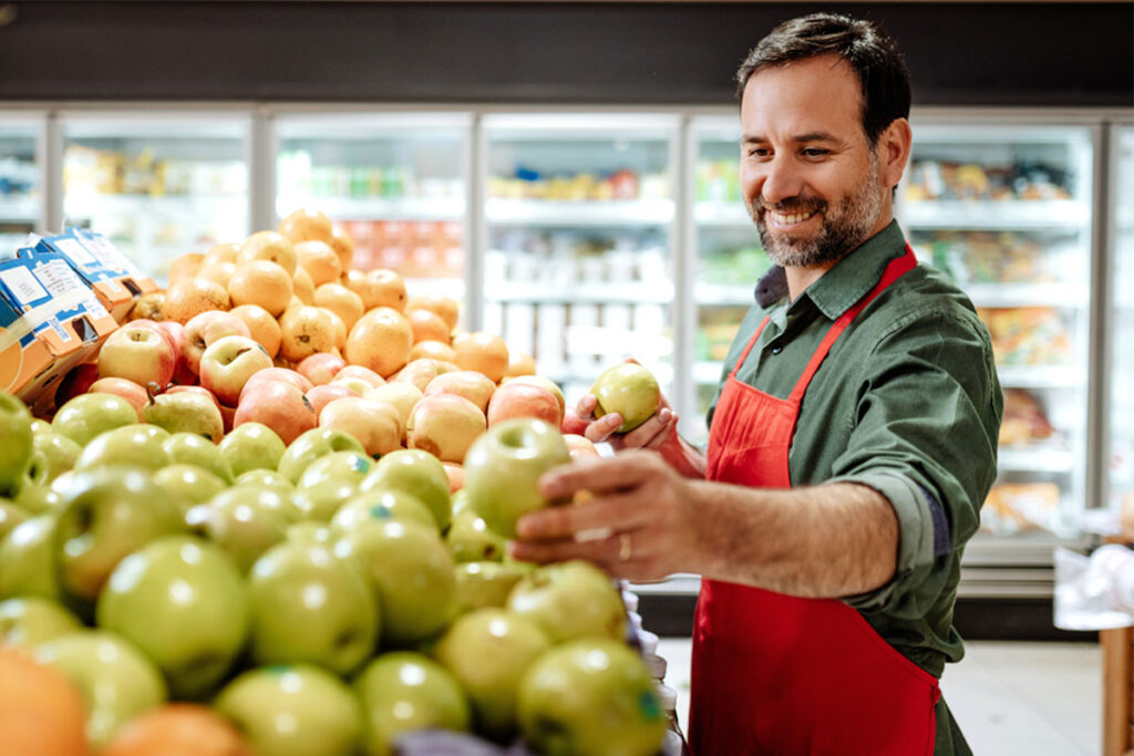 A man is stocking apples in a grocery store.