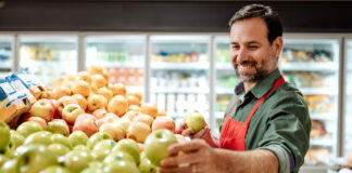 A man is stocking apples in a grocery store.