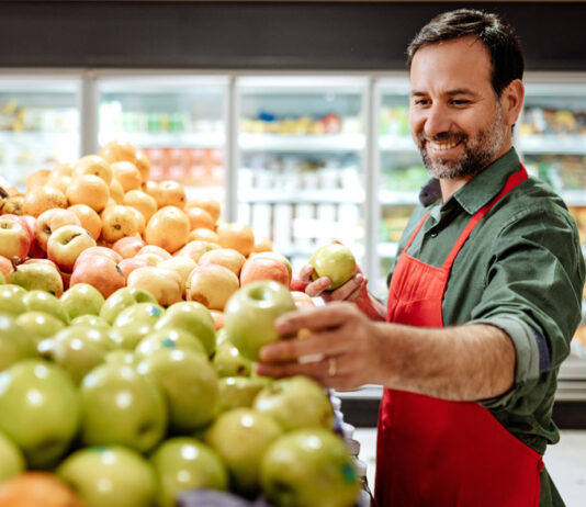 GroceryAid offers staff tips to survive the festive season A man is stocking apples in a grocery store.