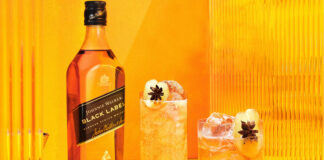 A bottle of Johnnie Walker Black Label is next to two cocktail serves set against an orange and yellow background.