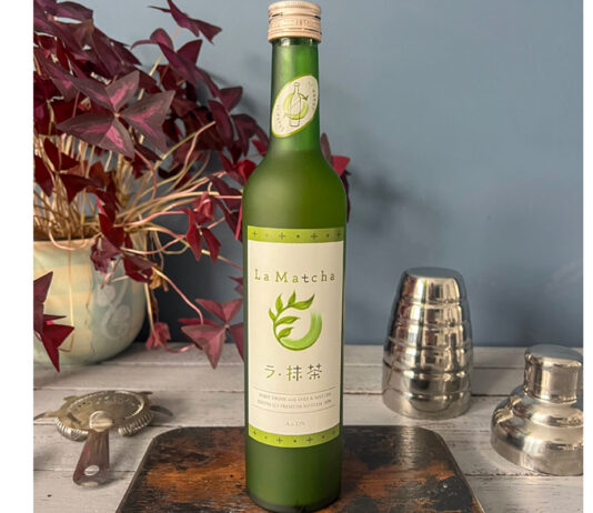Love Drinks expands La Liqueur A bottle of La Liqueur Matcha sits on a table with a wooden board beneath it and a disassembled cocktail shaker to its right and a potted plant to its left.