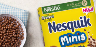 A cereal box of Nesquik Minis sits on table with a bowl filled with the cereal and a spoon next to the bowl.