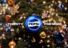 A Christmas tree with a blue bauble hanging from its branch with the Pepsi logo on it and surrounding text that reads "Thirsty For More".