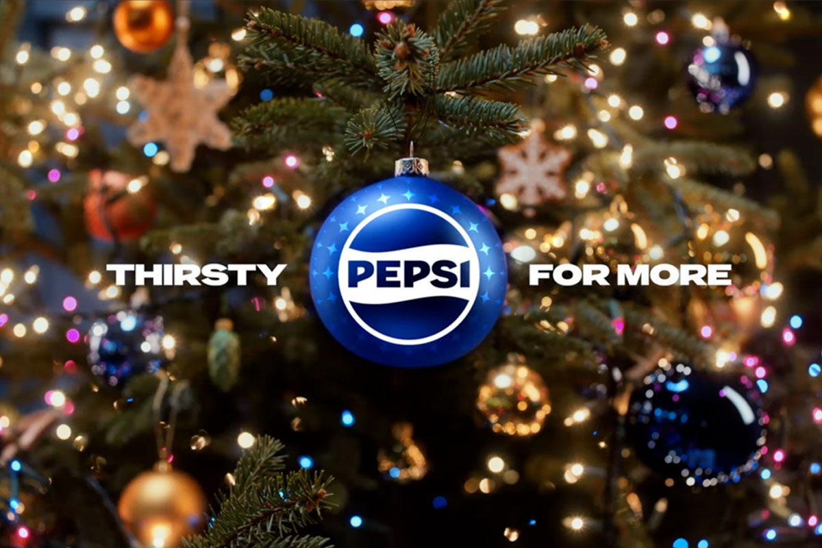 A Christmas tree with a blue bauble hanging from its branch with the Pepsi logo on it and surrounding text that reads "Thirsty For More".