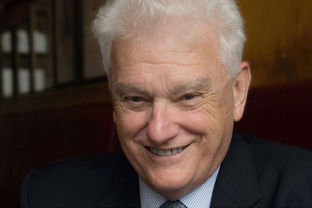 Ross Kerr smiles at a camera wearing a shirt and tie with a jacket.