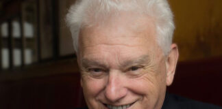 Ross Kerr smiles at a camera wearing a shirt and tie with a jacket.