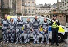 Team members from Scotmid dressed up in prisoner outfits as part of a charity fundraising efforts in front of a police van with an officer next to them.