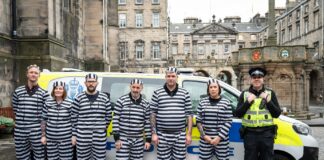 Team members from Scotmid dressed up in prisoner outfits as part of a charity fundraising efforts in front of a police van with an officer next to them.