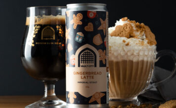 A can of Vault City Gingerbread Latte Stout stands on a table in front of a Vault City branded glass and a bowl with a gingerbread latte in it with whipped cream and gingerbread biscuit.