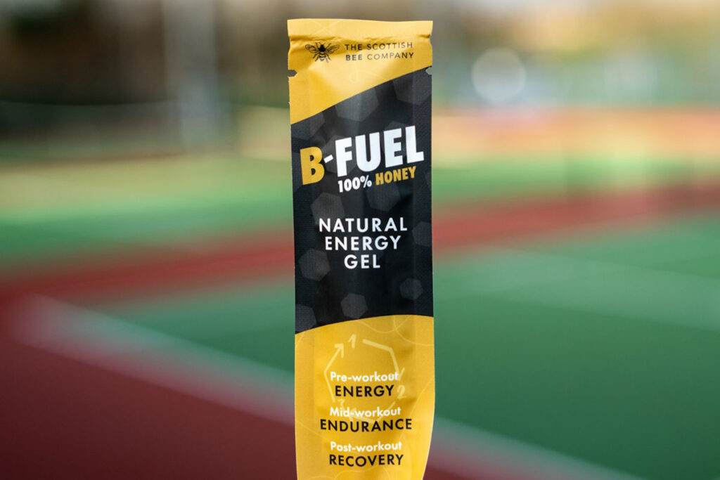 A packet of Scottish Bee B-Gel is held up against a blurred out field in the background.