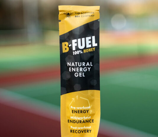Scottish Bee launches new B-Fuel honey sachets A packet of Scottish Bee B-Gel is held up against a blurred out field in the background.