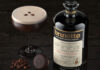 A bottle of Brunette Coffee Liqueur stands next to an Espresso Martini cocktail serve with coffee beans between the two.