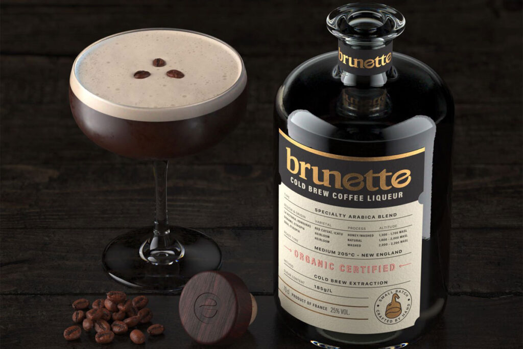 A bottle of Brunette Coffee Liqueur stands next to an Espresso Martini cocktail serve with coffee beans between the two.