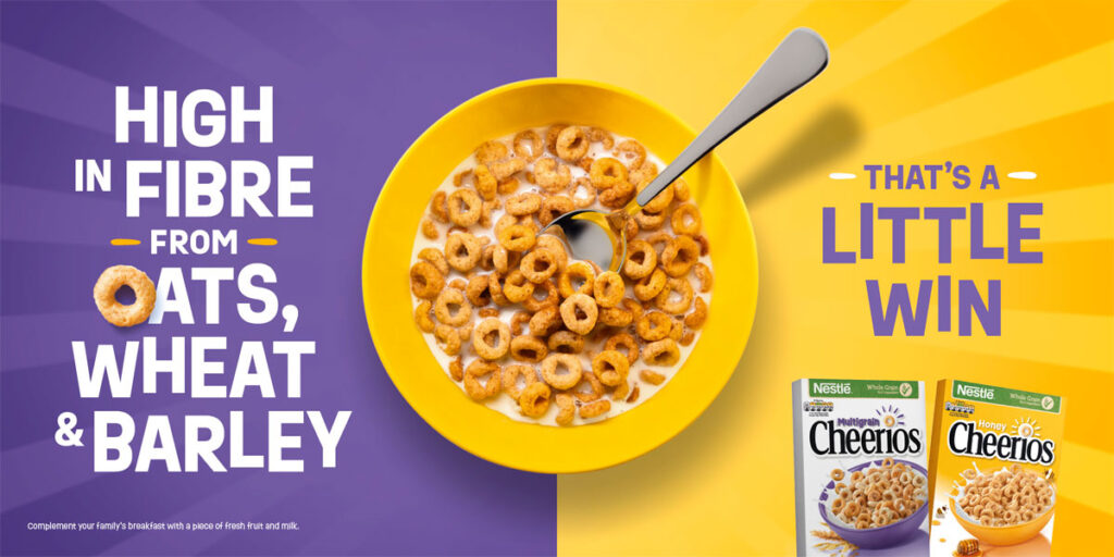 Advert for Cheerios TV campaign with a bowl of the cereal in the middle of a purple and yellow colour with the text to the left reading "High in Fibre from Oats, Wheat and Barley" with the text on the right reading "That's a little win" with boxes of Cheerios and Honey Cheerios beneath this text.