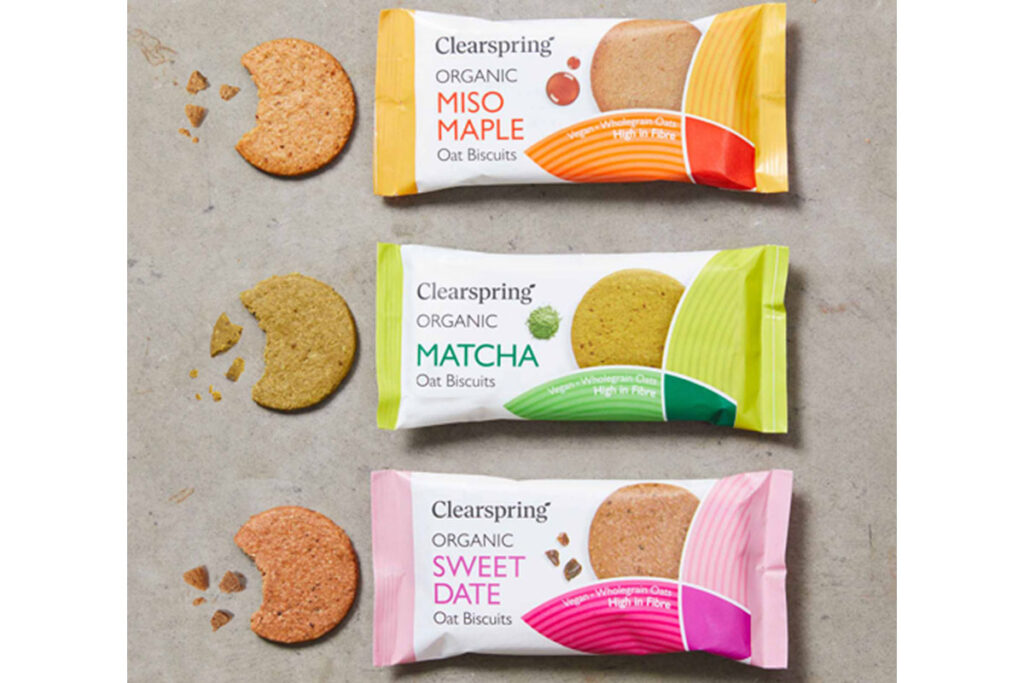 Packs of Clearspring Oat Biscuits sit against a grey background including Miso Maple, Matcha and Sweet Date with the biscuits sitting outside the packet with bites taken out of them.