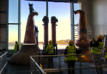 Stills being installed at Eden Mill Distillery with a large window in the background overlooking a waterfront landscape.