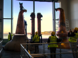 Eden Mill takes next step with new stills installed at distillery Stills being installed at Eden Mill Distillery with a large window in the background overlooking a waterfront landscape.