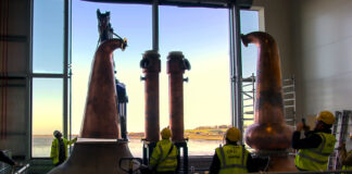 Stills being installed at Eden Mill Distillery with a large window in the background overlooking a waterfront landscape.