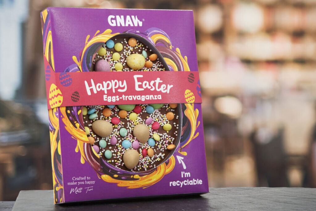 A pack of Gnaw Easter Happy Easter Eggs-travaganza stands upright on a table with a blurred out background.