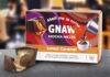 A pack of Gnaw Salted Caramel Mocha Melts sits on a table with one of the melts broken open with caramel pouring out next to the box.