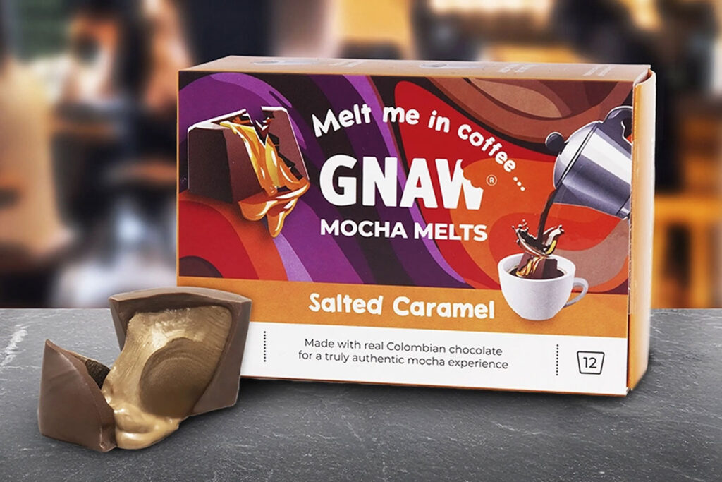 A pack of Gnaw Salted Caramel Mocha Melts sits on a table with one of the melts broken open with caramel pouring out next to the box.