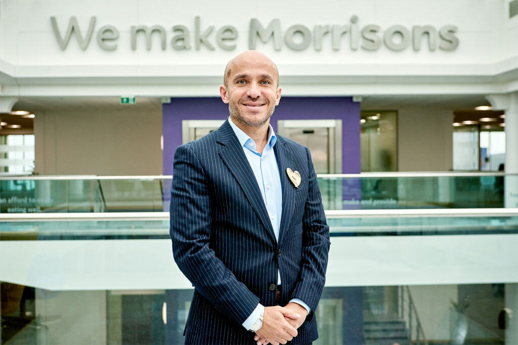 Rami Baitiéh, chief executive of Morrisons, stands in front of a sign that reads 'We make Morrisons' as he is appointed president of GroceryAid.