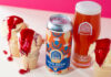 A can of Vault City Iron Brew Raspberry Ripple stands amongst ice cream cones with raspberry sauce with the beer poured into a Vault City branded glass.