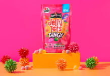 A packet of Jelly Tots Tangy stands on an orange platform against a pink background with spiky balls of different colours around the platform.