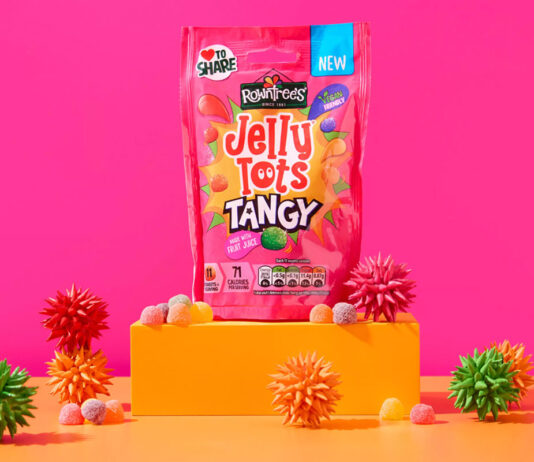 Rowntree’s celebrates with new Jelly Tots Tangy launch A packet of Jelly Tots Tangy stands on an orange platform against a pink background with spiky balls of different colours around the platform.