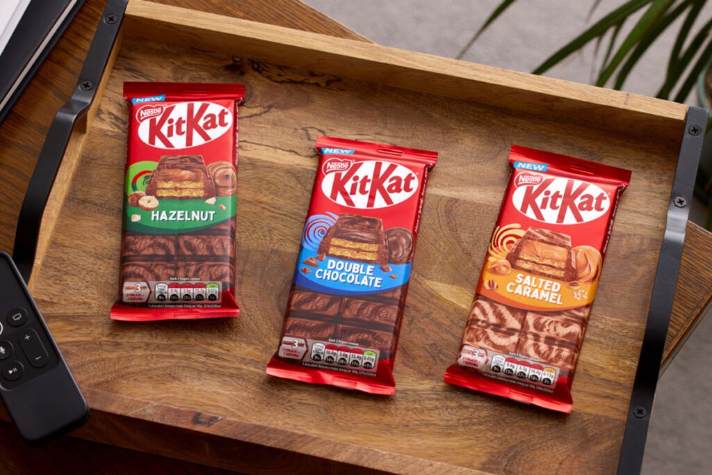 Packs of KitKat sharing bars sit on a wooden tray including KitKat Hazelnut, KitKat Double Chocolate and KitKat Salted Caramel.