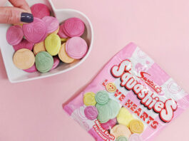 Swizzels spreads the Love with new Squashies variant A packet of Swizzels Squashies Love Hearts lies on a pink background with a heart-shaped bowl next to it with the sweets decanted into the bowl as a hand picks one out.