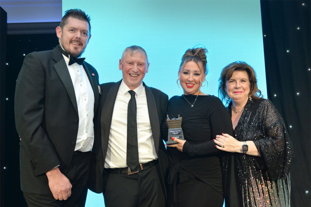 Tom Pook of Hovis, Dennis Williams and Sophi Williams of Premier Broadway Convenience store and actress Elaine C Smith stand on a stage at the Scottish Grocer Awards for the Community Store of the Year award win.