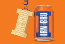 A can of Irn-Bru stands against an orange background with golden Irn-Bru Girder design hangs next to it, suspended by a drawing of a crane.