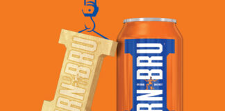 A can of Irn-Bru stands against an orange background with golden Irn-Bru Girder design hangs next to it, suspended by a drawing of a crane.