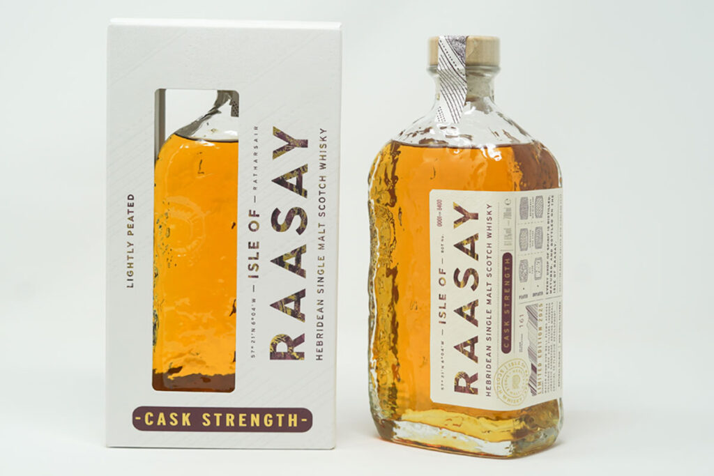 A bottle of Isle of Raasay Cask Strength Third Edition whisky stands next to the packaging for the whisky against a grey background.