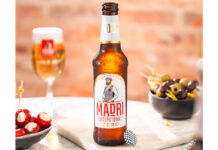 A bottle of Madrí Excepcional Zero stands on a table with a bowl of olives to the right and a bowl of cheese stuffed tomatoes to the left with a Madrí Excepcional branded glass behind the bottle.