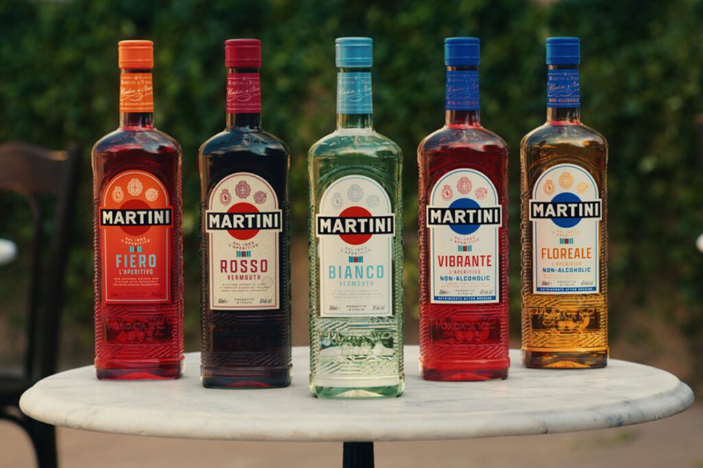 A line-up of Martini vermouth bottles stand on a marble table. (From left to right) Martini Fiero L'Aperitivo, Rosso Vermouth, Bianco Vermouth, Vibrante L'Aperitivo Vibrante Non-Alcoholic and Floreale L'Aperitivo Non-Alcoholic.