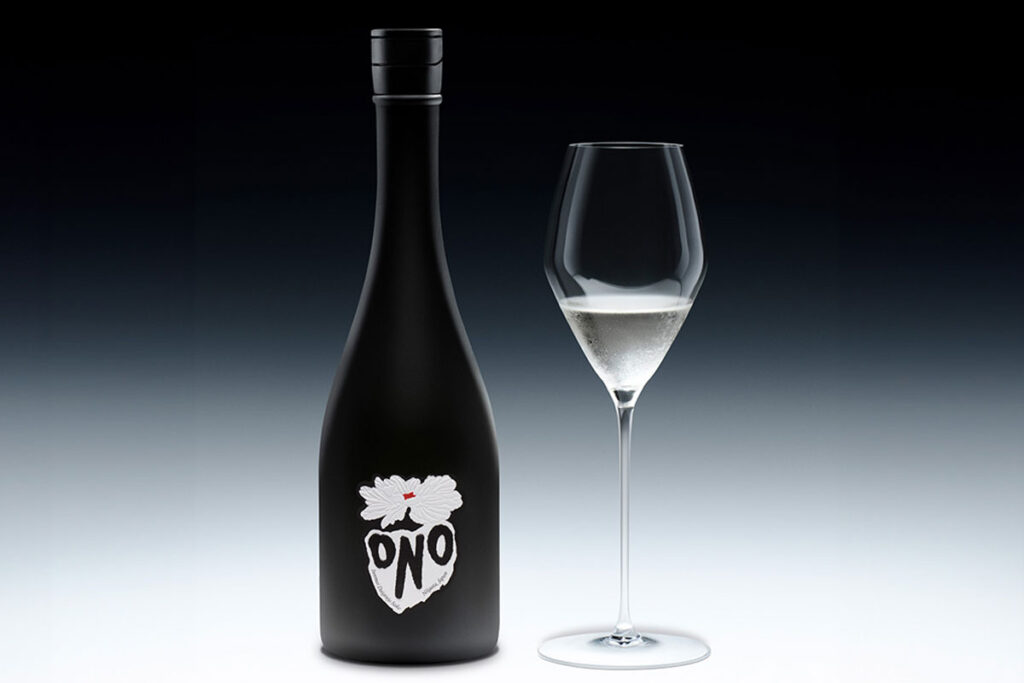 A bottle of Sake ONO stands against a black and white background with a wine glass next to it containing the spirit.