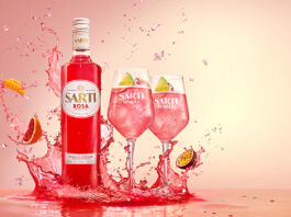 Sarti Rosa aperitif lands in the UK A bottle of Sarti Rosa splashes down in a liquid with two wine glasses next to it fill with the spirit and fruit, with pieces of fruit splashing into the liquid as well.