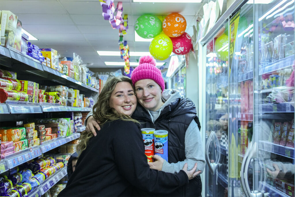 Sophie Williams stands with a customer inside Premier Broadway Convenience Store at the chillers, with balloons in the background with the number 40 on them.