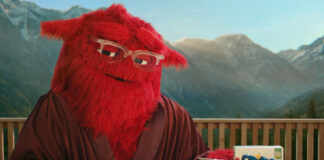 Alpen's mascot 'Mother' sits at a breakfast table with a box of Alpen, a jug for milk and a bowl of muesli in front of her. Mother is a large, red and furry character who wears glasses.