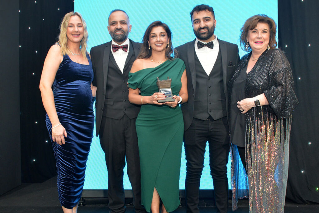 Laura McDiarmid, Vikas Sud, Shamly Sud, Guna Sud and Elaine C Smith all stand on the Scottish Grocer Awards 2024 stage whilst Shamly holds a trophy for The Innovation Award 2024.