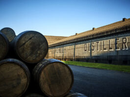 Bladnoch gives a ‘dram back’ to encourage exploration An exterior shot of the Bladnoch Distillery featuring whisky barrels stacked up in the foreground of the image with the distillery's warehouse in the background with the words Bladnoch Distillery across the side of the warehouse wall.