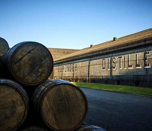 Bladnoch gives a ‘dram back’ to encourage exploration An exterior shot of the Bladnoch Distillery featuring whisky barrels stacked up in the foreground of the image with the distillery's warehouse in the background with the words Bladnoch Distillery across the side of the warehouse wall.