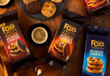 Packets of Fox's Fabulous biscuits sit on a table with biscuits placed onto plates with a mug of coffee between two packs of the biscuits – the biscuit variants include Half Coated Dark Chocolate Cookies, Half Coated Milk Chocolate Cookies, Milk Chocolate Cookies.