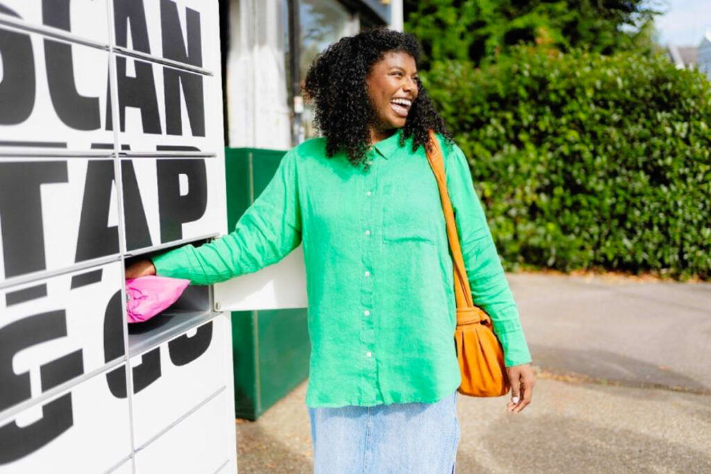 A woman in a green jumper is placing a parcel in an InPost branded lockers to be delivered.