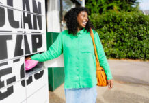 A woman in a green jumper is placing a parcel in an InPost branded lockers to be delivered.