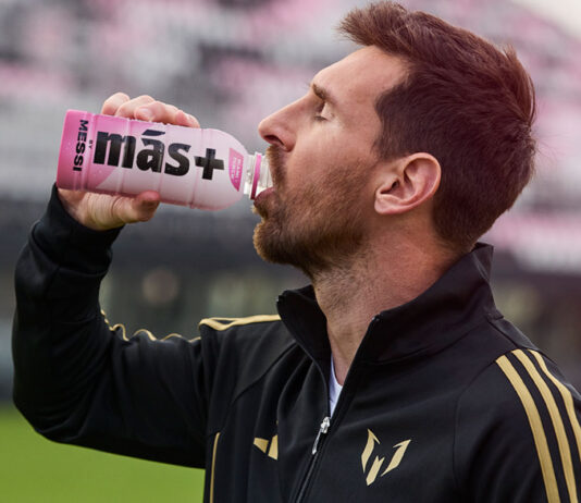 Messi launches Más+ by Messi drinks exclusively in Spar Lionel Messi drinks from a Mas+ by Messi Miami Punch drink in a football stadium.